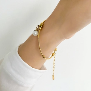 Detail of adjustable gold pearl bracelet on model wrist with minimalist white sleeve