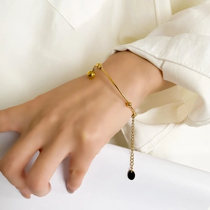 Detail of a gold pearl bracelet on a wrist featuring an adjustable chain and gold beads