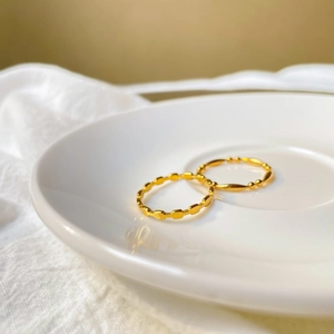 Détail d'une bague carrée dorée élégante et d'un anneau perlé sur une assiette en céramique