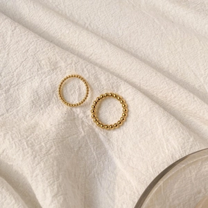 Detail of two minimalist gold-plated beaded rings on a textured off-white linen surface