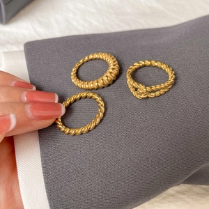 Gros plan d'un lot de trois bagues dorées torsadées sur un tissu gris élégant