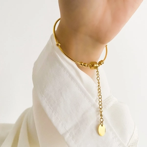 Close-up of minimalist gold pearl bangle with hanging pendant on a female wrist