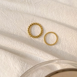 Macro detail of two minimalist gold beaded stackable rings on white fabric texture