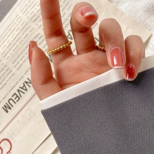 Gros plan de bagues torsadées dorées portées sur des ongles dégradés corail chic