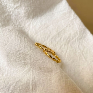 Détail d'une bague perlée en or 18K minimaliste sur un fond de lin blanc doux