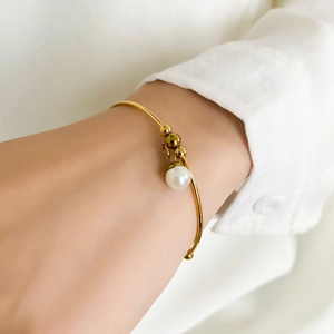Close-up of minimalist gold cuff bracelet featuring round beads and a white pearl charm