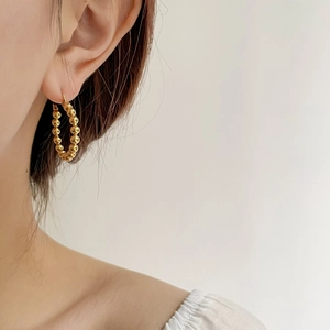 Close-up of a minimalist gold beaded hoop earring worn by a model in soft lighting