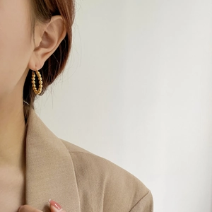 Detailed view of a gold beaded hoop earring worn by a model in a minimalist style