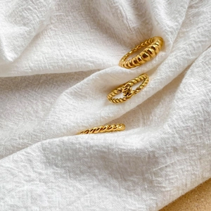 Détail de trois bagues dorées torsadées posées sur un tissu blanc texturé minimaliste