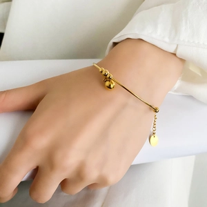 Detail of adjustable gold minimalist bangle featuring floating beads and a round charm