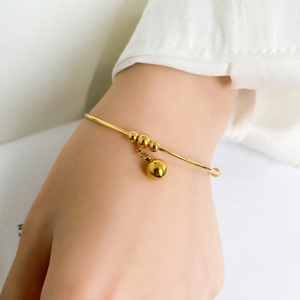 Detail of a minimalist gold bracelet featuring three beads and a solid spherical charm