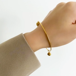 Close-up of minimalist gold-plated open cuff bracelet with polished metal beads
