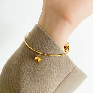 Detail of a minimalist gold open bangle with a polished metal bead charm on wrist