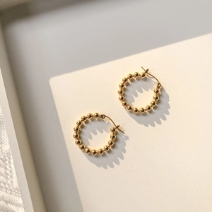 Detail shot of minimalist gold beaded hoop earrings featuring polished metallic spheres