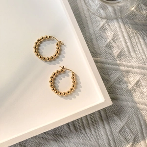 Close-up of golden beaded hoop earrings on white tray with soft knit background texture