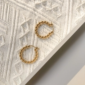Detailed close-up of golden beaded hoop earrings resting on white textured fabric
