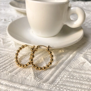 Minimalist gold beaded hoop earrings shown on a white ceramic saucer with textured fabric