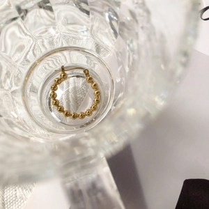 Detailed view of golden beaded hoop earring with textured finish on glass surface