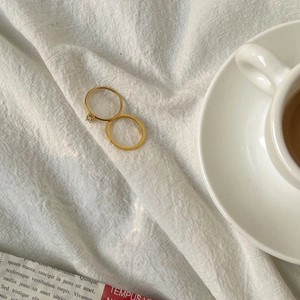 Detail of 18K gold plated titanium rings with zircon inlay on soft white fabric background