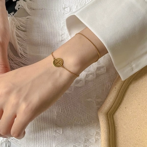 Detail of a thin gold snake chain bracelet with a hollow circular Fu character charm