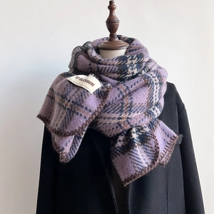 Détail d'une écharpe à carreaux lilas avec bordures marron et étiquette sur manteau