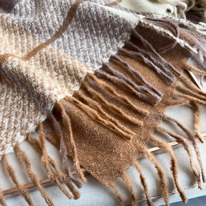 Close-up of thick plaid cashmere-like scarf showing earth-tone knit texture and tassels