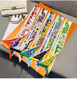 Detail of colorful printed silk twilly scarves arranged on an orange gift box with handbag