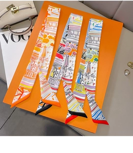Close-up of three colorful illustrated twilly scarves displayed on an orange luxury board