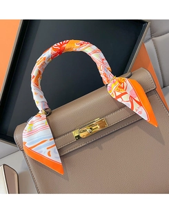 Detail of printed orange silk scarf wrapped on a taupe leather handbag handle