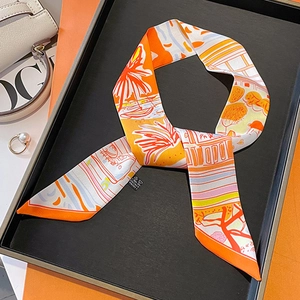 Close-up of orange printed twilly scarf on a display tray with a white leather handbag