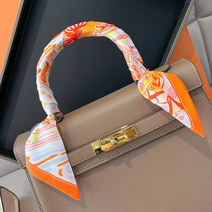 Detail of printed silk scarf wrapped on grey leather handbag handle with gold buckle
