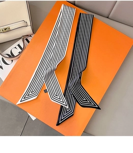 Détail de foulards twilly en satin à rayures noires et blanches sur fond orange vif