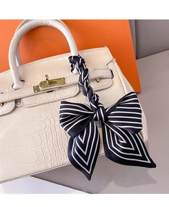 Détail d'un foulard en soie rayé noir et blanc noué en nœud sur l'anse d'un sac blanc