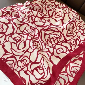Elegant off-white scarf with red rose pattern and fine twill texture shown on dark leather