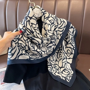 Classic black and white rose print scarf shawl with camellia pendant on a brown sofa