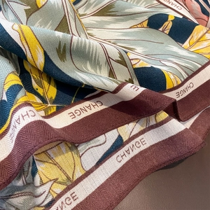 Silk-textured scarf featuring tropical leaf prints and decorative CHANGE lettering border