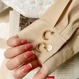 Detail of gold croissant-style twisted rope C-shaped stud earrings on khaki fabric
