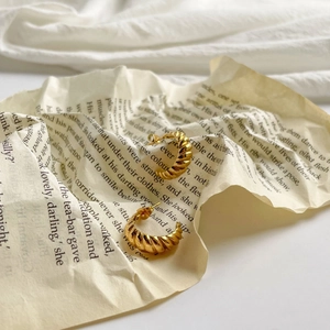 Close-up of golden croissant-style stud earrings with spiral texture on book page