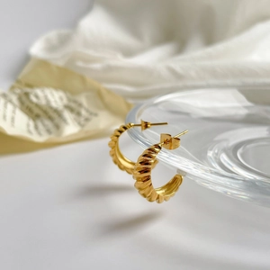 Macro detail of gold croissant twist hoop earrings on a transparent glass edge