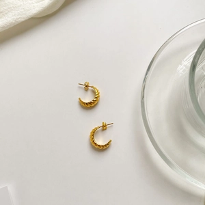 Close-up of golden croissant-style twisted hoop earrings on a minimalist white backdrop