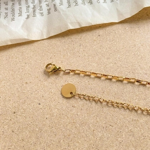 Detail of gold geometric chain with lobster clasp and round tag on retro background