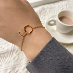 Detail of interlocking golden double rings on a delicate chain bracelet against a knit background