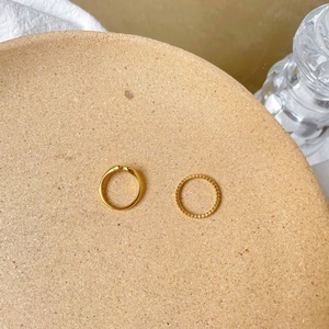 Minimalist gold V-shape and textured stackable ring set on a rustic cork tray surface