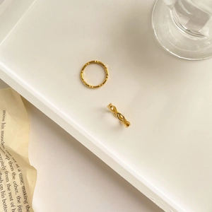 Détail de bagues dorées texturées bambou et corde sur un plateau blanc avec journal