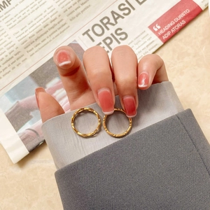 Gros plan de bagues ondulées minimalistes en métal doré portées avec un fond de journal