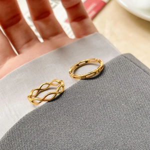 Détail de deux bagues dorées avec motifs géométriques évidés sur un tissu gris doux