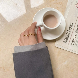 Gros plan de bagues dorées à nœud infini et anneau lisse portés avec une tasse de café
