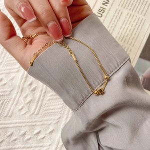 Close-up of golden box chain bracelet with K18 engraving and geometric beads detail