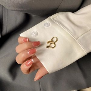 Détail de boucles d'oreilles créoles dorées étoile et lune sur une manche de chemise