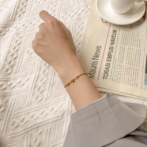 Close-up of minimalist gold beaded titanium steel bracelet worn on a wrist over knitwear